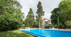 Ein Schwimmbad, umgeben von üppiger Vegetation und einem Gebäude mit einem Ziegeldach.