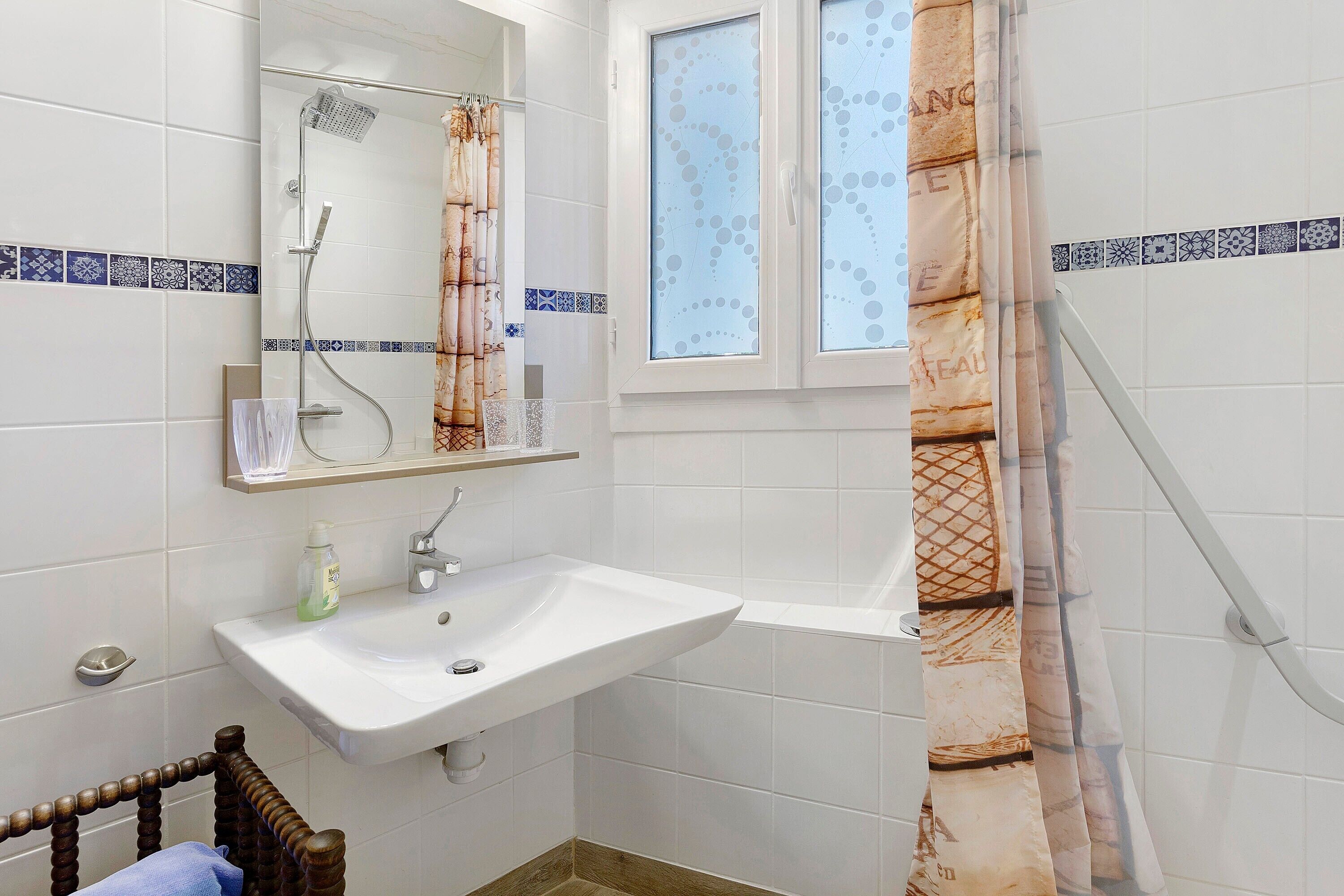 Baño con lavamanos blanco, espejo, ducha y ventana con cortinas estampadas.