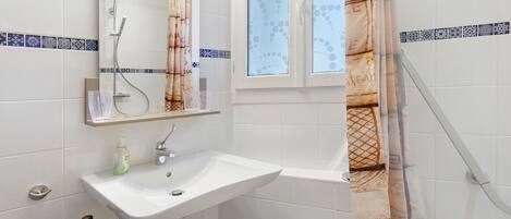Baño con lavamanos blanco, espejo, ducha y ventana con cortinas estampadas.