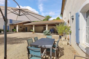 Eine Terrasse mit Tisch und Stühlen, eine Pergola mit Vordach und ein Gebäude mit Ziegeldach.