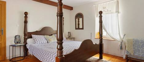 A bedroom with a four-poster bed, a nightstand, a mirror, and a window with curtains.
