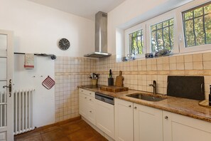 Eine Küche mit doppelter Spüle, einem Herd, einer Uhr und einem Fenster mit Blick auf Bäume.