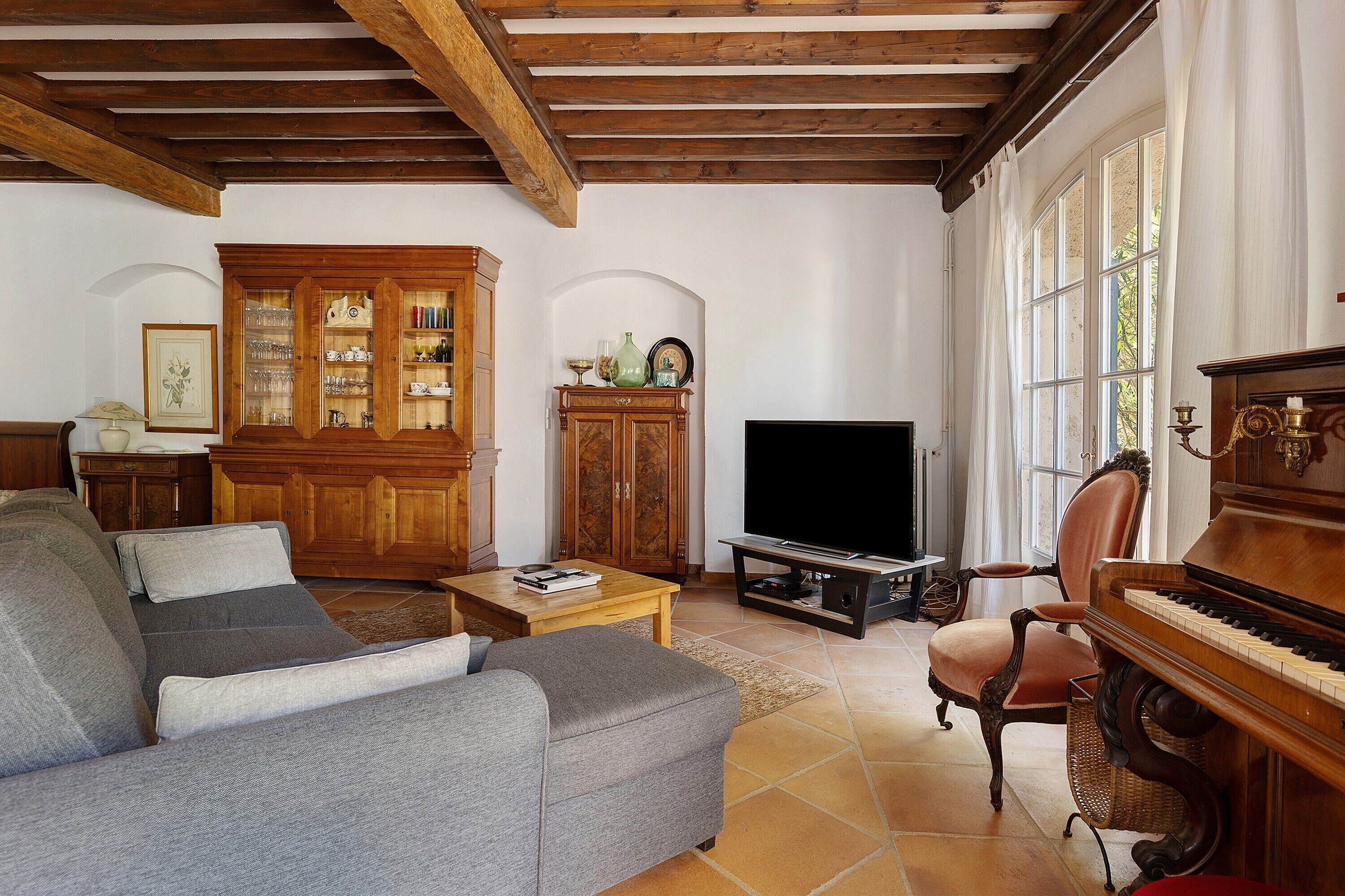 A living room with a sofa, a television, a piano, and a cabinet with glass doors.