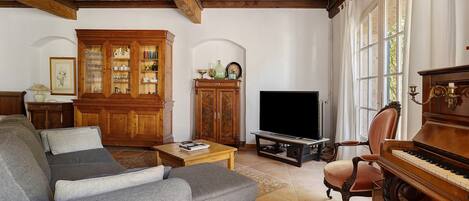 A living room with a sofa, a television, a piano, and a cabinet with glass doors.