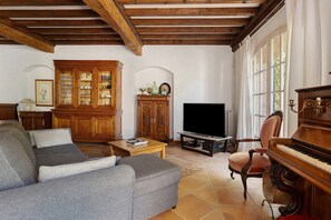 A living room with a sofa, a television, a piano, and a cabinet with glass doors. - Holiday home 'Gîte Palmier - Le Trabet' with pool in the heart of the vineyards (Moussoulens)