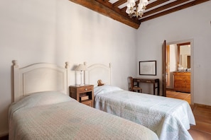 Ein Zimmer mit zwei Betten, einem Nachttisch mit Lampe, einem Stuhl, einem Schreibtisch mit Stuhl und einem Spiegel an der Wand.