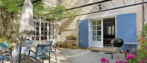 Ein Terrassenbereich im Freien mit Tisch und Stühlen, einem Grill und einer überdachten Sitzgruppe mit Tisch und Stühlen.