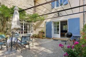 Un espace extérieur aménagé en patio, avec une table et des chaises, un barbecue et un coin salon couvert, également équipé d’une table et de chaises.