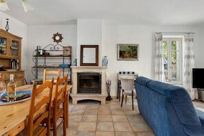 Ein Wohnzimmer mit Kamin, einem Essbereich mit Holztisch und -stühlen, einem blauen Sofa und einem Fernseher.