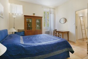 A bedroom with a bed, a desk, a chair, a wardrobe, and a window with curtains. - Domaine Le Trabet - Gîte Laurier (Moussoulens)