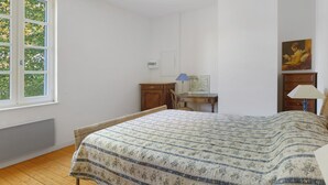 Ein Schlafzimmer mit einem Bett, einem Schreibtisch, einem Stuhl und einem Fenster mit Blick auf Bäume.