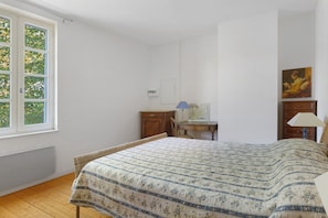 Ein Schlafzimmer mit einem Bett, einem Schreibtisch, einem Stuhl und einem Fenster mit Blick auf Bäume.