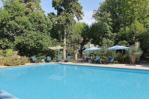 A swimming pool with lounge chairs and umbrellas, surrounded by trees. - Domaine Le Trabet - Gîte Laurier (Moussoulens)