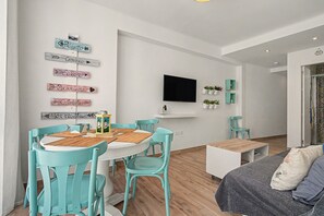A modern living room with a dining area, a flat-screen TV mounted on the wall, and a small table with chairs. - Apartment 'Playa Torrecilla' with Sea View, Wi-Fi and Air Conditioning (Nerja)