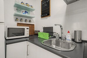 Eine Küche mit Mikrowelle, Spüle und Regalen voller Küchenutensilien.