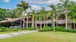 A multi-story resort with thatched-roof structures, lush tropical vegetation, and a paved walkway. - Tortuga C17Luxury Villa Punta Cana  (Higüey)