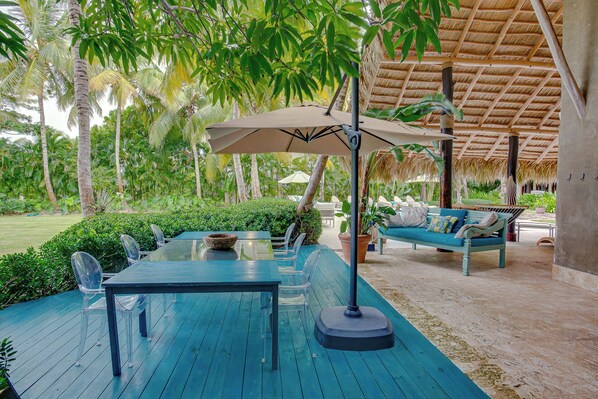 Un espace extérieur aménagé avec une table et des chaises, un banc et une structure dotée d’un toit de chaume.