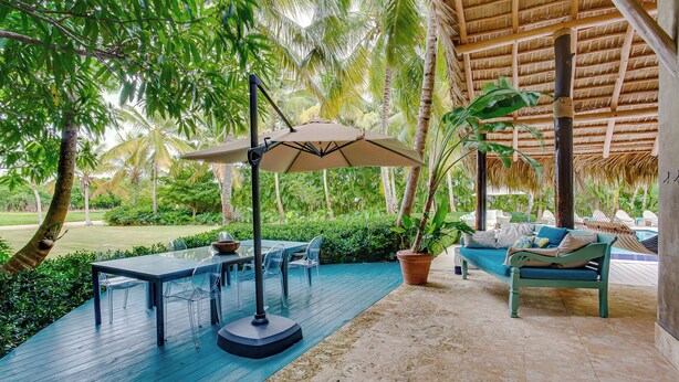 An outdoor patio with a table, chairs, a sofa, and a thatched roof structure. - Tortuga C17Luxury Villa Punta Cana  (Higüey)