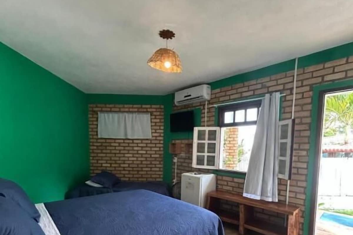 A bedroom with a bed, a bench, a window with curtains, and an air conditioning unit.