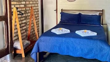 A bedroom with a brick wall, a bed with blue bedding, two wall-mounted fans, and a wooden ladder.