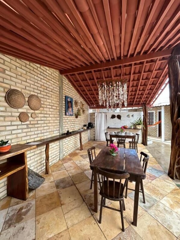 An outdoor patio with a brick wall, wooden ceiling, and a dining table with chairs. - Pousada Ventoria (Canguaretama)