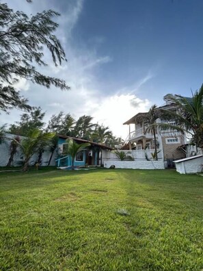 A grassy yard with a house, a small shed, and a palm tree. - Pousada Ventoria (Canguaretama)