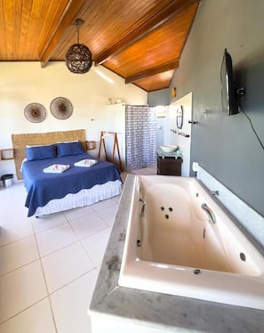 A bedroom with a large bed, a bathtub, and a wooden ceiling. - Pousada Ventoria (Canguaretama)