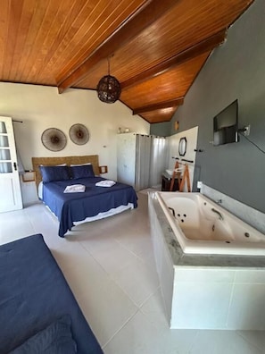 A bedroom with a bed, a bathtub, and a wooden ceiling. - Pousada Ventoria (Canguaretama)