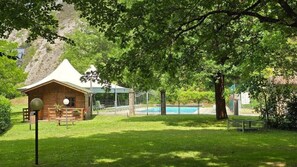 Una cabana de fusta amb teulada verda, una piscina i un arbre gran al primer pla.
