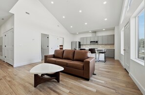A spacious living area with a brown leather sofa, a white coffee table, and a kitchen with grey cabinets and a microwave. - Two Bottles Inn - Palisade Wine Country Retreat Signature Suite Balcony 7 (Palisade)