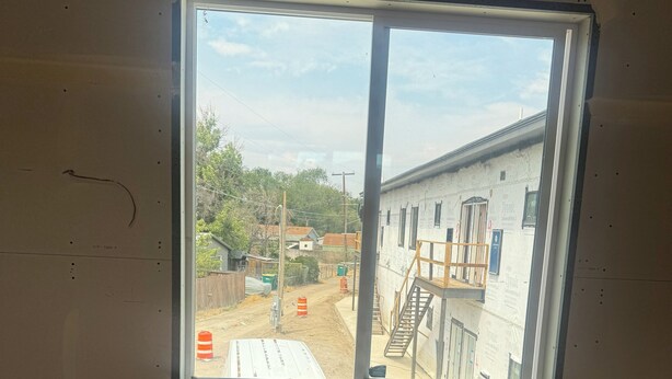 A room with a large window, a white wall, and a visible construction site outside.
