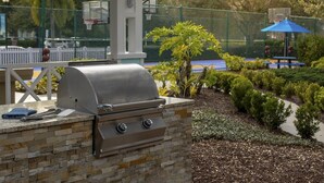 An outdoor grill area with a stone wall, a basketball hoop, and a blue umbrella. - 1 Bedroom Villa at Harbour Lake Family-Friendly (ORLANDO)