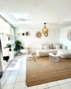 A modern living room with a sofa, a round coffee table, and a large woven rug. - Stunning 2-bedroom apartment on the waterfront in Cap d'Agde (Le Cap d Agde)