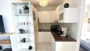 Une cuisine compacte avec des meubles blancs, un four à micro-ondes, un grille-pain et un petit îlot central doté d’un évier.