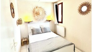 Une chambre à coucher comprenant un lit, un ventilateur de plafond, deux lampes fixées au mur, un miroir décoratif et une petite table de chevet.