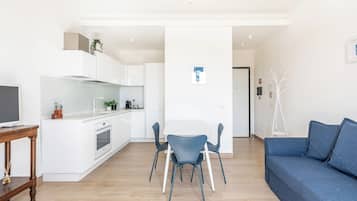 Una cocina moderna con armarios blancos, un comedor con sillas azules y un sofá azul.