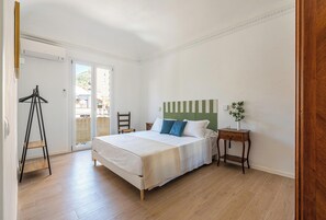 A bedroom with a bed, a nightstand, a chair, a wooden floor, and a balcony. - Igiea Florio Sea View Apartments by Wonderful Italy (Palermo)