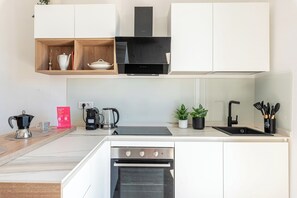 A modern kitchen with white cabinetry, a black range hood, a built-in oven, a coffee maker, and a sink. - Igiea Florio Sea View Apartments by Wonderful Italy (Palermo)