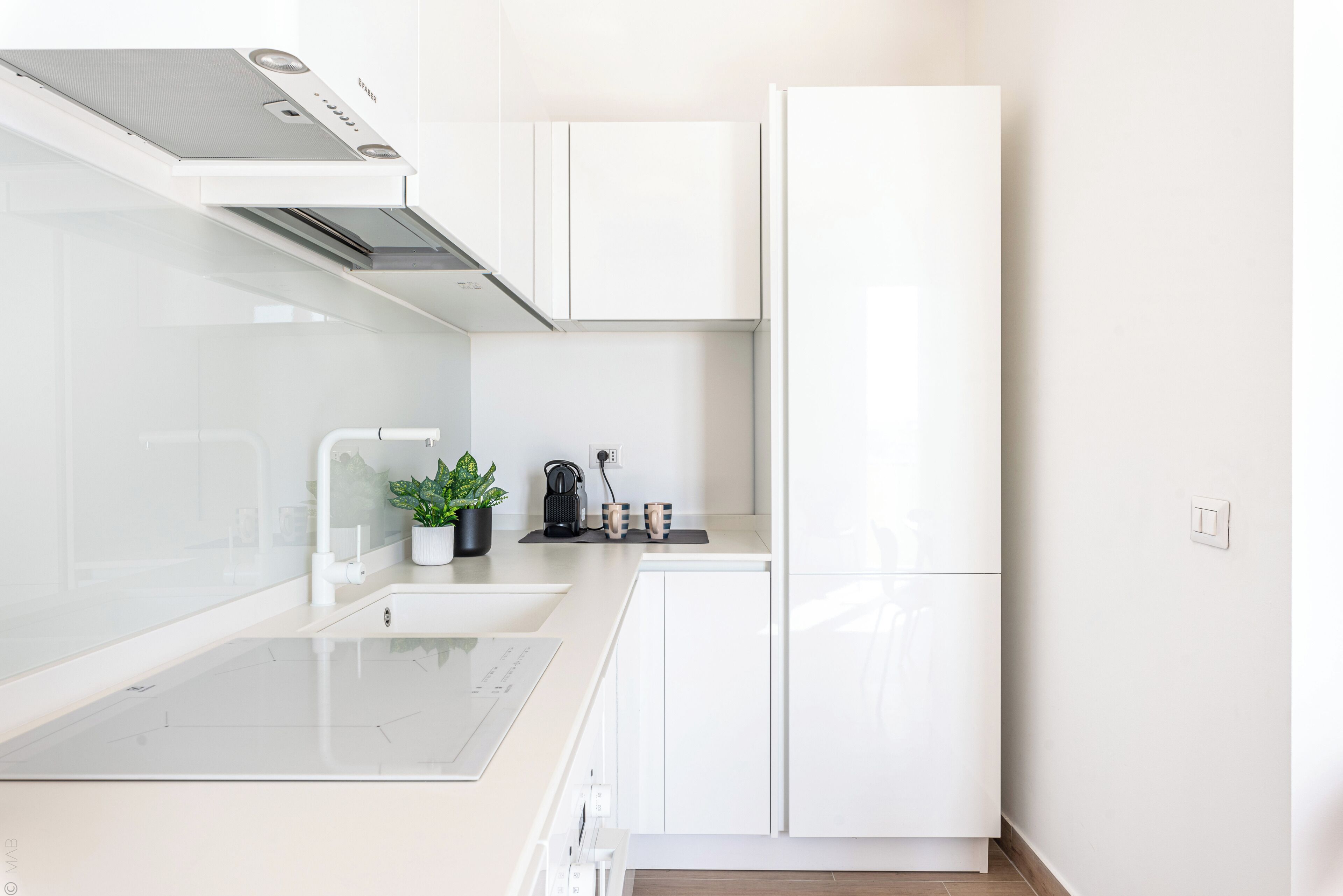 Una cocina moderna con muebles blancos, estufa empotrada y un lavamanos.