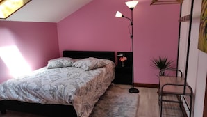A bedroom with a bed, a floor lamp, a hanging light, a plant, and a metal rack.