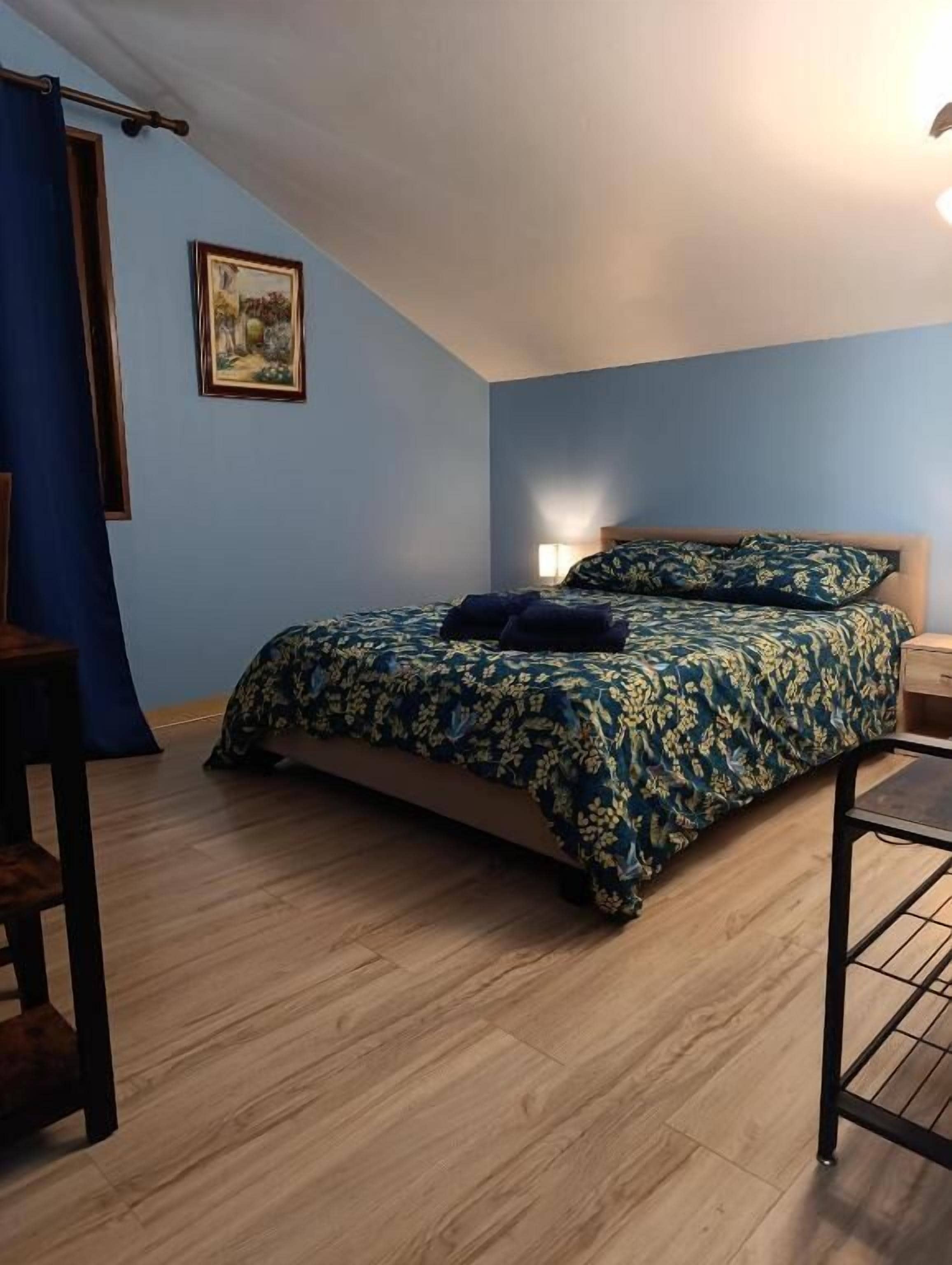 Un dormitorio con cama, escritorio, silla, lámpara y un cuadro en la pared.