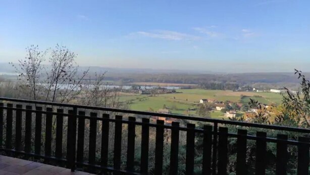 A balcony with a view of a rural landscape, including fields and a distant body of water.