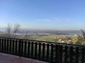 Un balcone con vista su un paesaggio rurale, che comprende campi e un corpo d'acqua in lontananza.