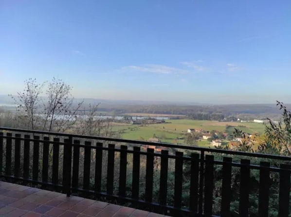 Un balcón con vistas a un paisaje rural, incluyendo campos y una masa de agua distante.