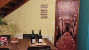 A dining area with a wooden table, chairs, and a wine bottle. There is a staircase in the background and a door with a mural.