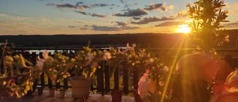 Une vue sur le coucher de soleil depuis un balcon agrémenté de plantes en pot et d’une balustrade.