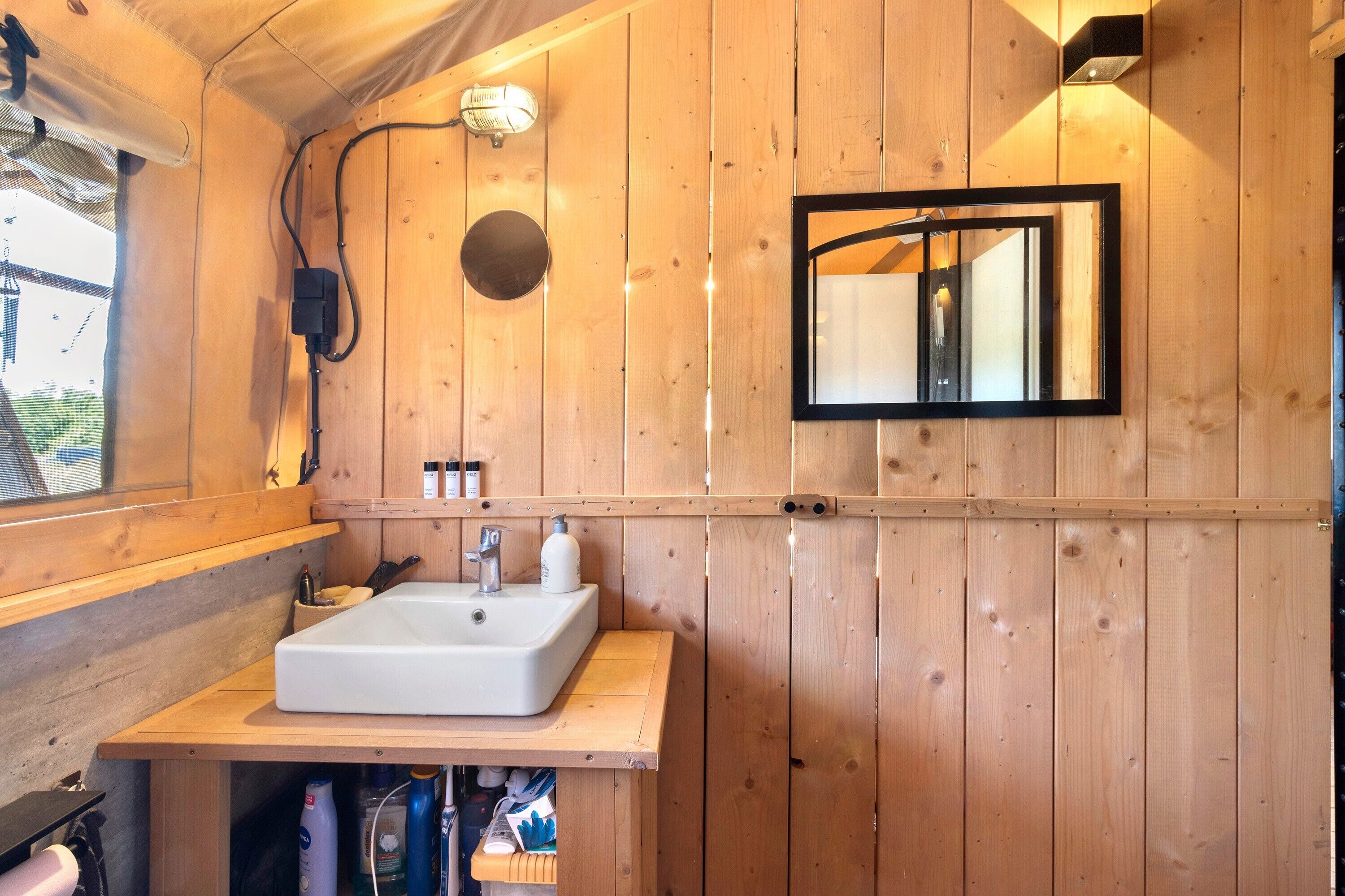 Baño de cabaña de madera con lavamanos, espejo y repisa con artículos de aseo.