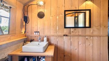 Baño de cabaña de madera con lavamanos, espejo y repisa con artículos de aseo.