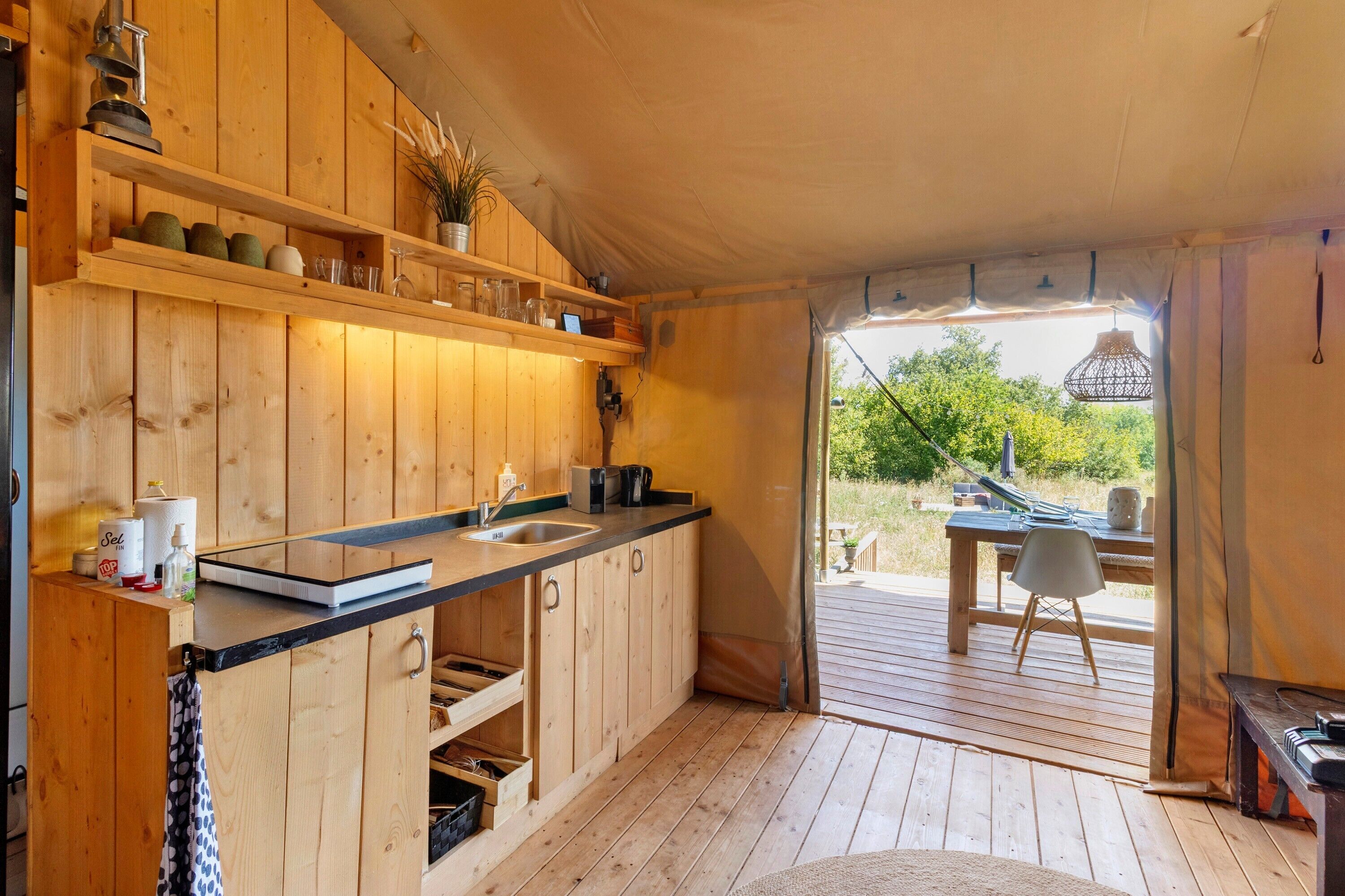 Eine kleine Küche mit Holzschränken, einer schwarzen Arbeitsplatte und einem Spülbecken. Draußen befindet sich ein Essbereich mit Tisch und Stühlen.