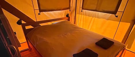 A single bed with a headboard and footboard, a wooden floor, and a window with a curtain.